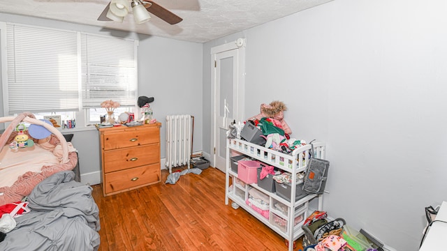 bedroom with ceiling fan, radiator heating unit, wood-type flooring, and a textured ceiling