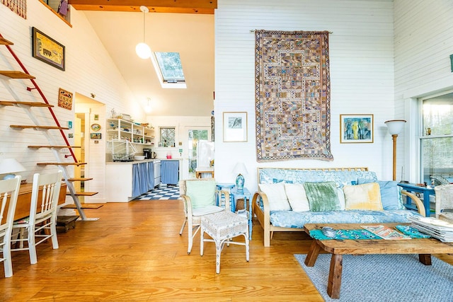 living room featuring a skylight, high vaulted ceiling, and light hardwood / wood-style flooring