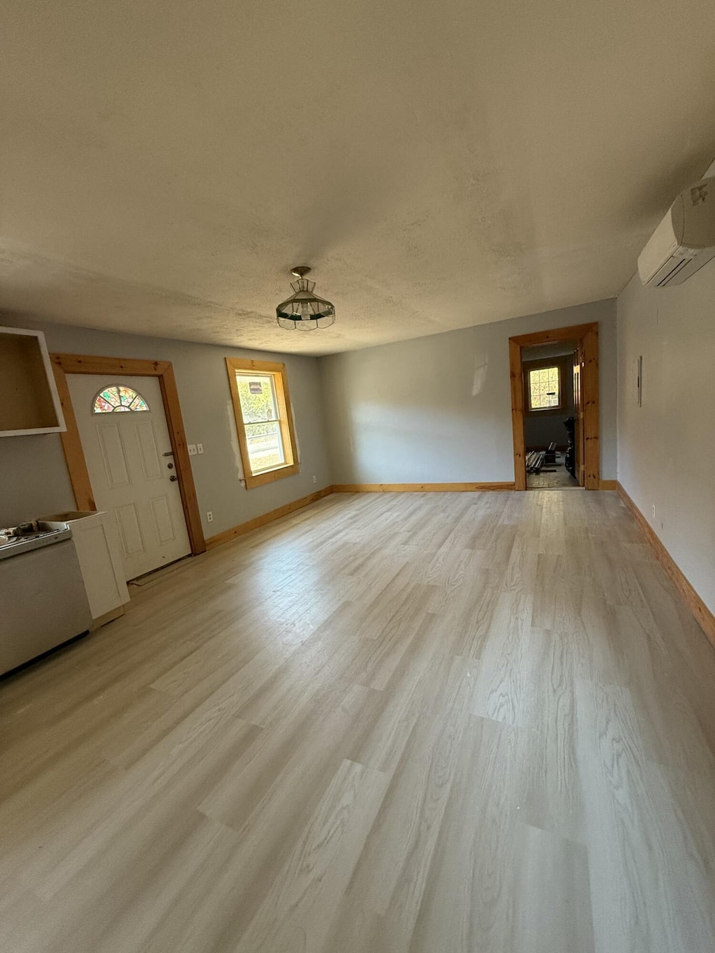 unfurnished living room with light hardwood / wood-style floors, a textured ceiling, and a wall mounted AC