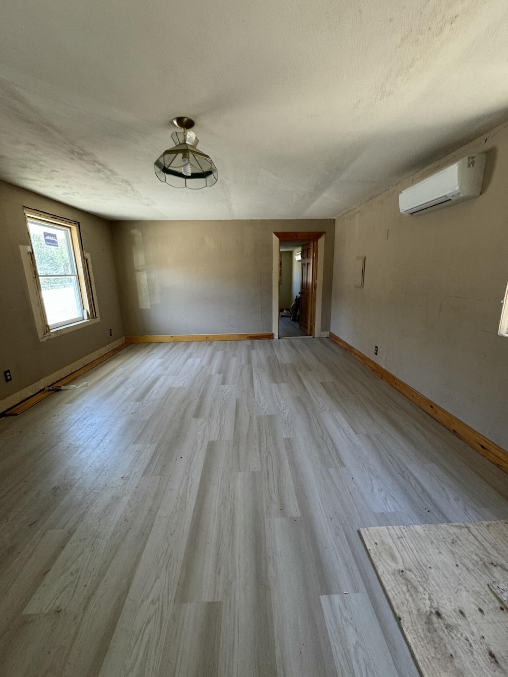 unfurnished room with a wall mounted AC, light hardwood / wood-style flooring, and a textured ceiling