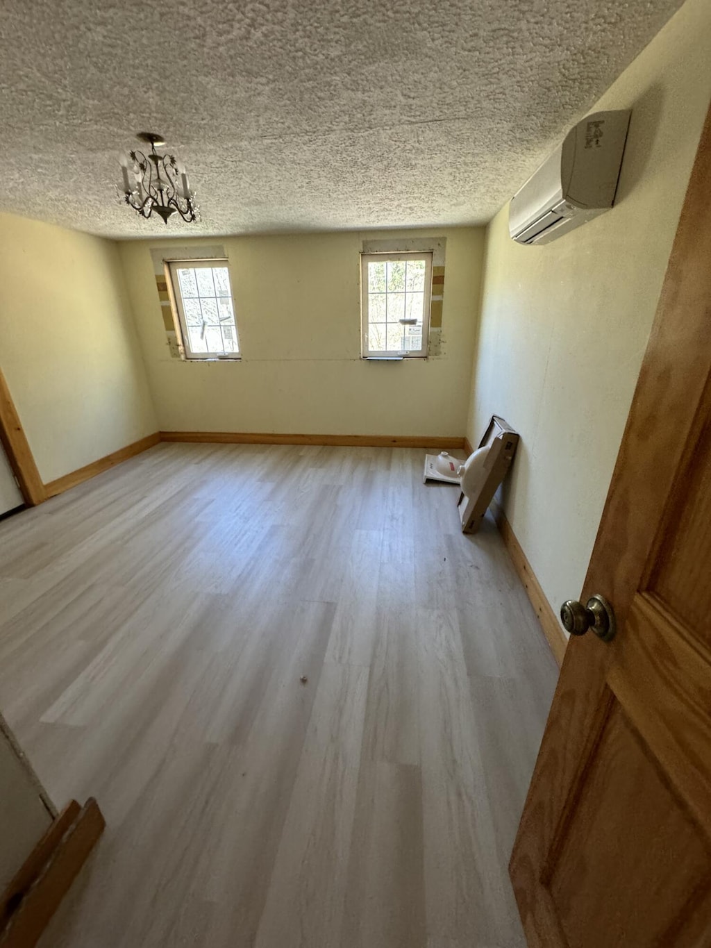 spare room with a wall mounted air conditioner, plenty of natural light, a notable chandelier, and light hardwood / wood-style flooring