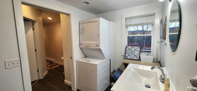 laundry area featuring dark wood-type flooring, stacked washing maching and dryer, a baseboard heating unit, and sink