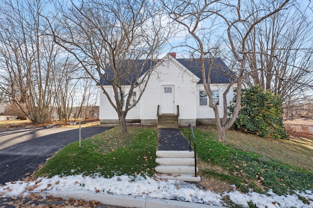 bungalow-style house featuring entry steps, roof with shingles, and a chimney