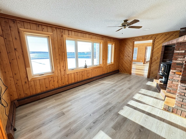 unfurnished living room with ceiling fan, a baseboard radiator, a water view, light hardwood / wood-style floors, and a wood stove