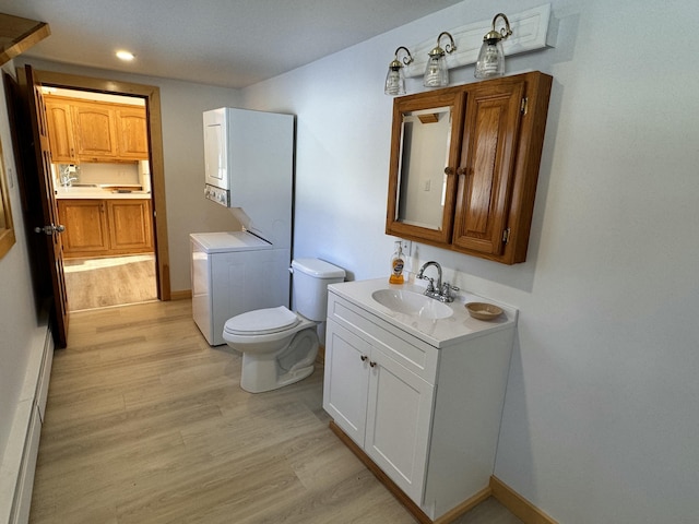 bathroom featuring a baseboard heating unit, stacked washer / dryer, hardwood / wood-style floors, toilet, and vanity