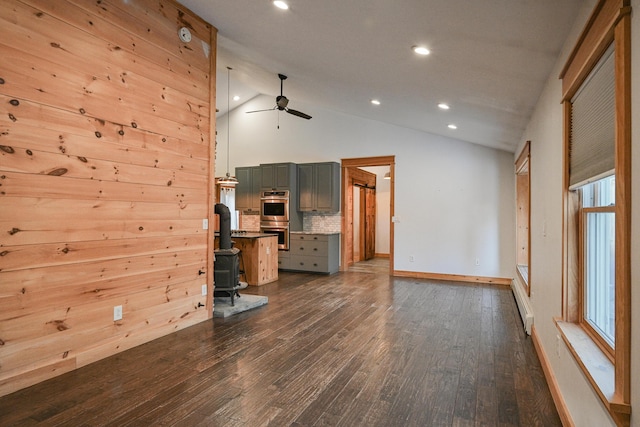 unfurnished living room with high vaulted ceiling, a wood stove, dark hardwood / wood-style flooring, and ceiling fan