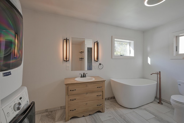 bathroom with a bathtub, stacked washer / drying machine, vanity, and toilet