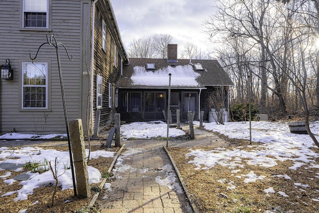 snow covered back of property featuring a sunroom