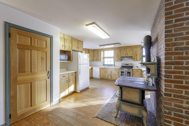 kitchen with ventilation hood, light wood-type flooring, white appliances, and a wood stove