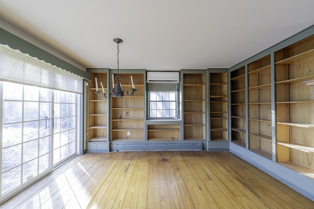 unfurnished dining area featuring a healthy amount of sunlight, hardwood / wood-style flooring, an AC wall unit, and a notable chandelier