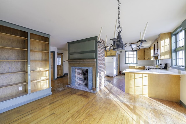 kitchen featuring white refrigerator, light hardwood / wood-style floors, a fireplace, and kitchen peninsula