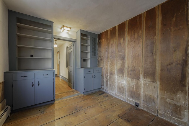 interior space featuring a baseboard heating unit, built in features, light hardwood / wood-style floors, and wood walls