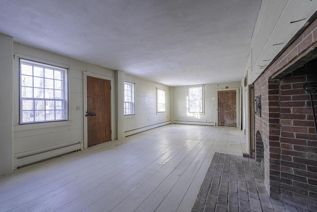 unfurnished living room with a wealth of natural light, a baseboard heating unit, and light hardwood / wood-style flooring