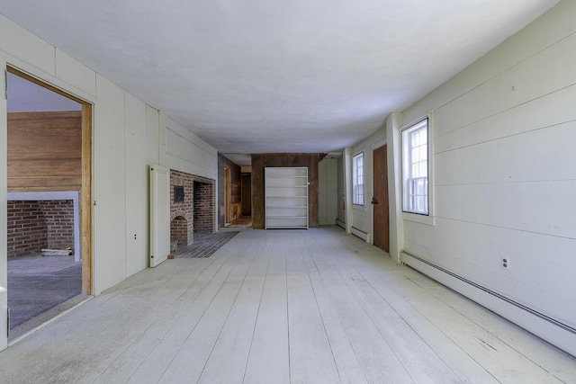 unfurnished living room featuring a baseboard heating unit, a fireplace, wood walls, and light hardwood / wood-style floors