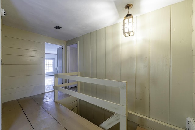 corridor with a baseboard radiator and wooden walls