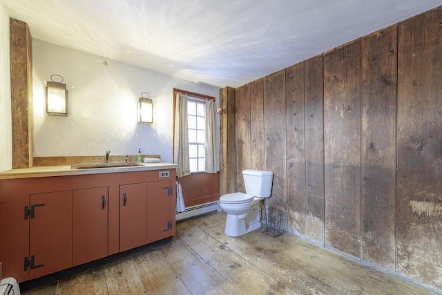 bathroom with toilet, vanity, wood walls, wood-type flooring, and a baseboard radiator