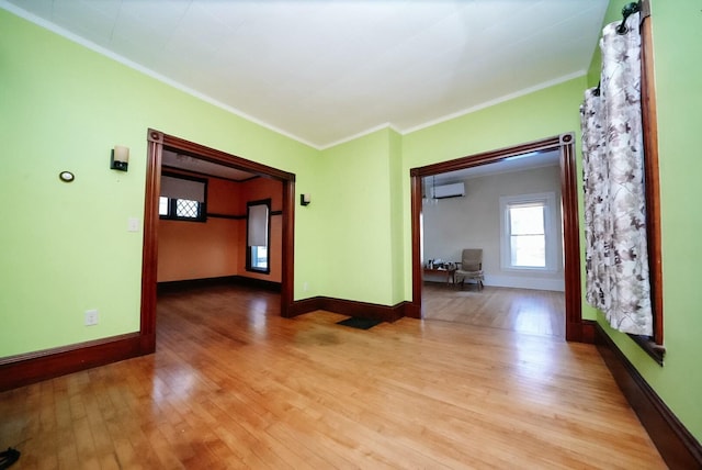 empty room with light hardwood / wood-style floors, a wall mounted air conditioner, and ornamental molding