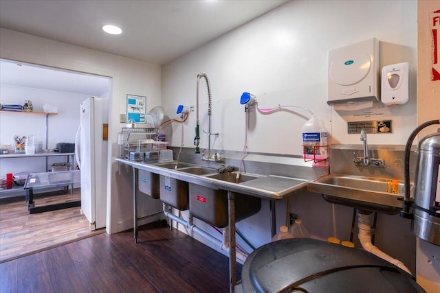 kitchen with stainless steel counters, white fridge, sink, and dark wood-type flooring