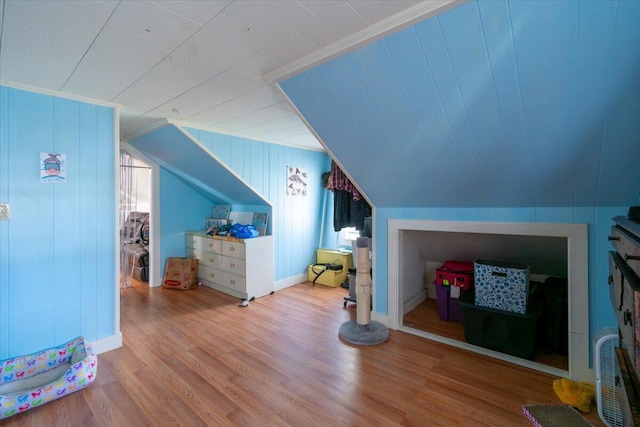 bonus room with vaulted ceiling, light hardwood / wood-style flooring, and wood walls