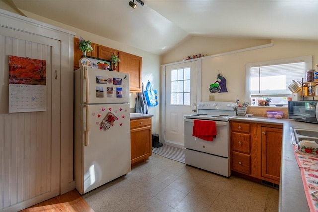 kitchen with vaulted ceiling, wood walls, sink, and white appliances