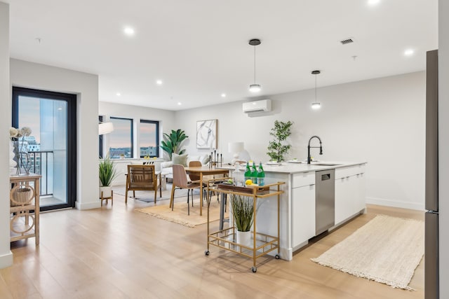 kitchen featuring sink, hanging light fixtures, stainless steel dishwasher, white cabinetry, and a wall unit AC