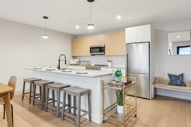 kitchen with sink, hanging light fixtures, stainless steel appliances, an island with sink, and decorative backsplash