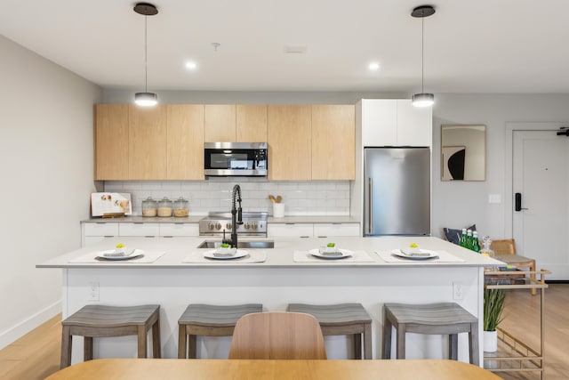 kitchen featuring appliances with stainless steel finishes, tasteful backsplash, a center island with sink, and pendant lighting