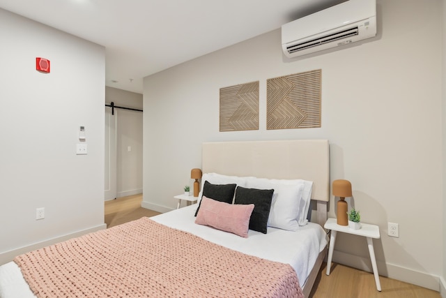 bedroom featuring a barn door, light hardwood / wood-style floors, and a wall mounted air conditioner