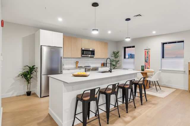 kitchen featuring sink, an island with sink, decorative light fixtures, white cabinetry, and stainless steel appliances