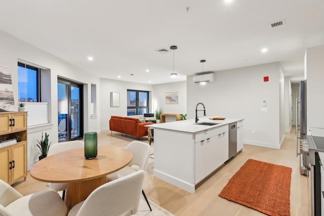 kitchen featuring dishwasher, sink, a wall mounted AC, decorative light fixtures, and a kitchen island with sink