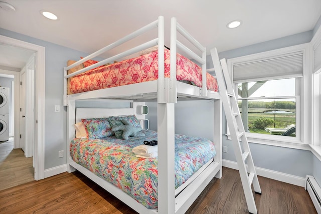 bedroom with stacked washer and dryer, dark wood-type flooring, and a baseboard heating unit