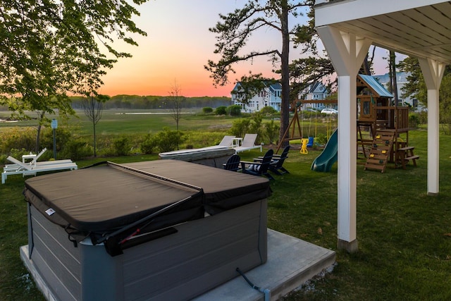 yard at dusk featuring a playground and a hot tub