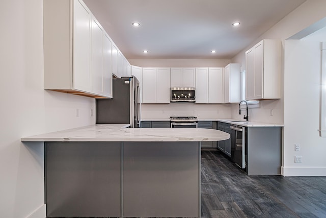 kitchen with kitchen peninsula, appliances with stainless steel finishes, dark hardwood / wood-style flooring, white cabinetry, and a breakfast bar area