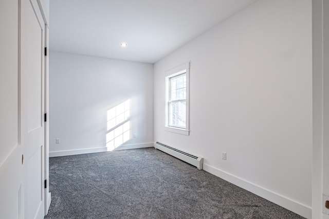 empty room featuring baseboard heating and dark colored carpet