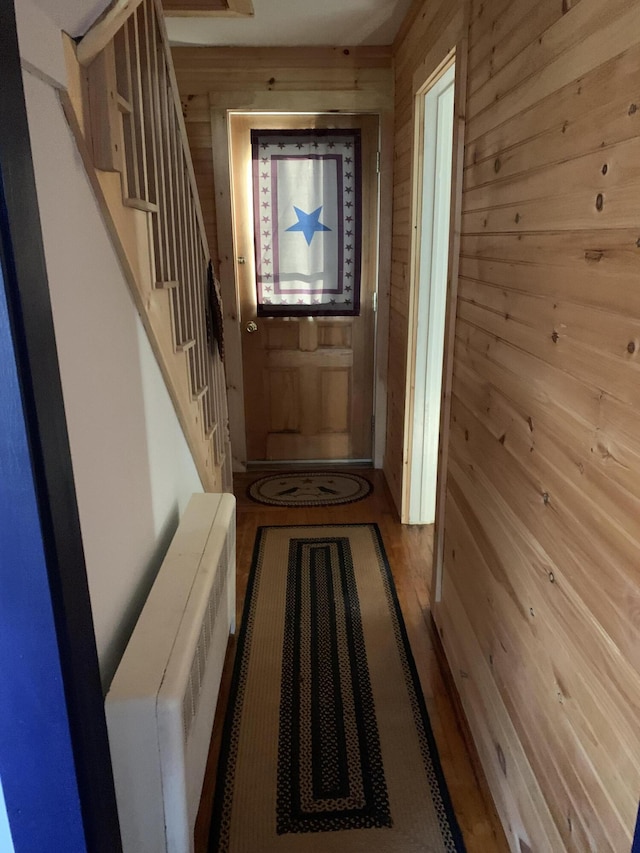 doorway to outside with hardwood / wood-style floors, radiator, and wooden walls