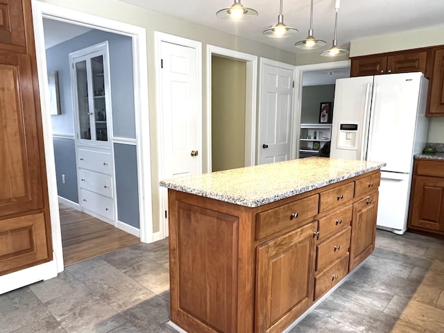 7 Edgewood Dr, Orono, ME 04473 - kitchen with white fridge with ice dispenser, hanging light fixtures, a center island, light stone countertops, and brown cabinetry