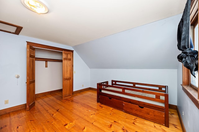 bedroom featuring light hardwood / wood-style floors, vaulted ceiling, and a closet