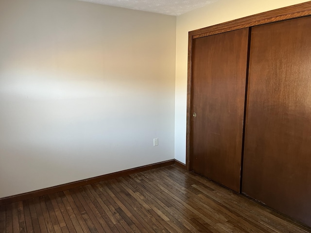 unfurnished bedroom featuring a textured ceiling, dark hardwood / wood-style flooring, and a closet