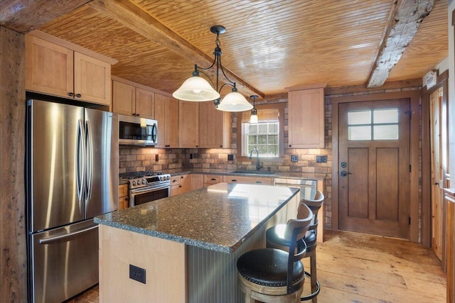 kitchen with appliances with stainless steel finishes, dark stone counters, sink, light hardwood / wood-style flooring, and a center island