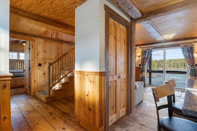 corridor featuring beamed ceiling, light hardwood / wood-style flooring, wooden ceiling, and wood walls