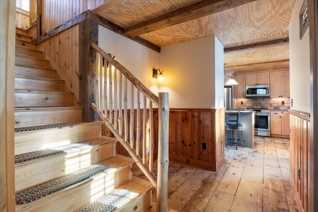 stairs with wooden walls, hardwood / wood-style floors, beamed ceiling, and wood ceiling