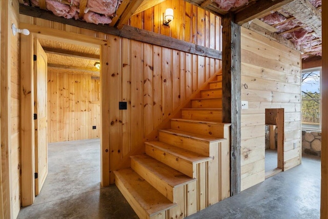 stairway featuring wood walls and concrete floors