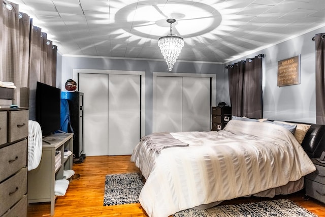 bedroom featuring multiple closets, crown molding, light hardwood / wood-style flooring, and a notable chandelier