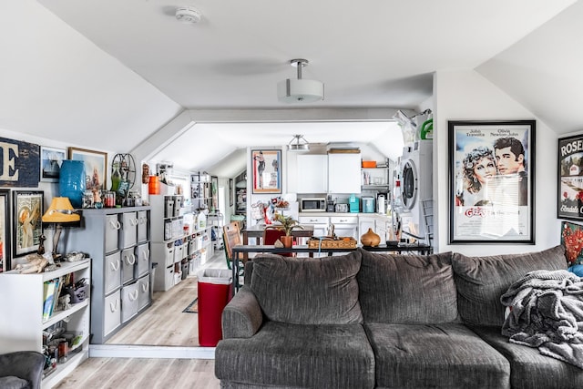 living room featuring lofted ceiling, light wood-type flooring, and stacked washing maching and dryer