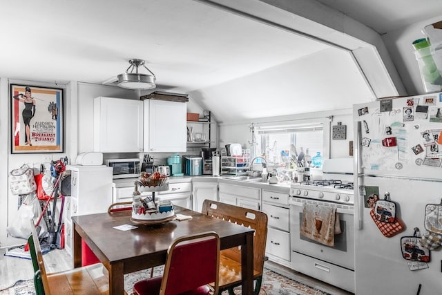 kitchen with white appliances, white cabinetry, vaulted ceiling, and sink