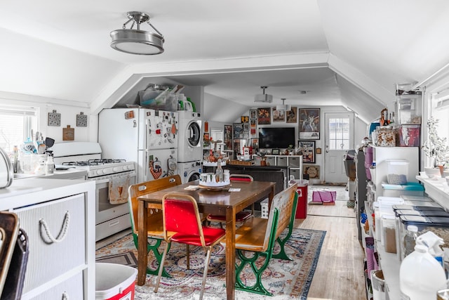 kitchen with lofted ceiling, white appliances, light hardwood / wood-style flooring, and stacked washer and clothes dryer