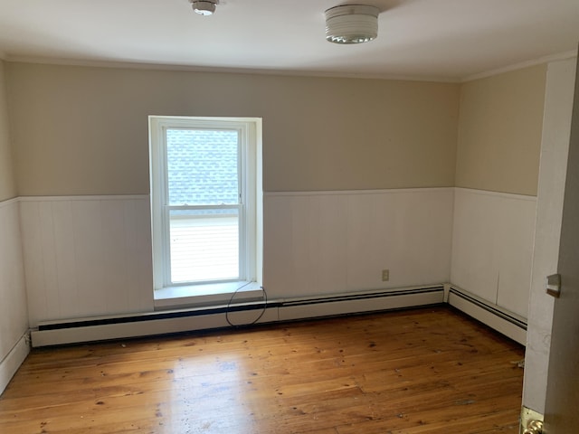 spare room featuring baseboard heating, hardwood / wood-style floors, and ornamental molding