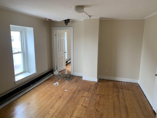 empty room featuring wood-type flooring, a baseboard radiator, and crown molding