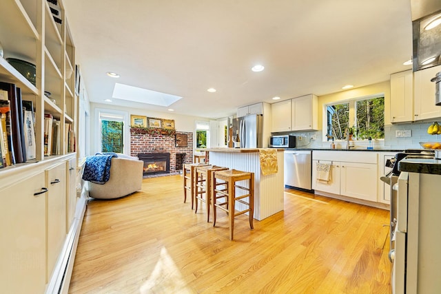 15 Brentwood Dr Unit 4, Cumberland, ME 04110 - kitchen featuring appliances with stainless steel finishes, a kitchen bar, a brick fireplace, light wood-type flooring, and a skylight