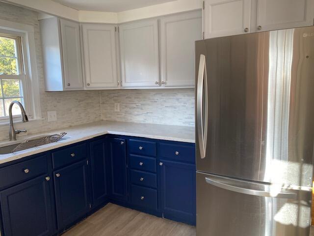 kitchen featuring sink, light hardwood / wood-style flooring, blue cabinets, stainless steel fridge, and white cabinets